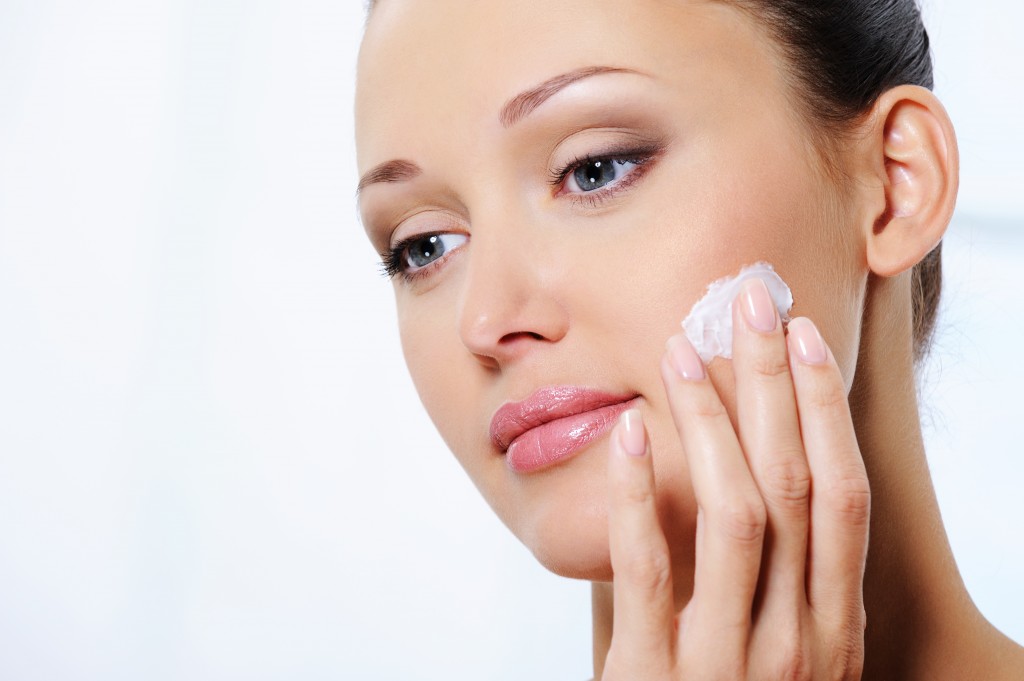 Young beautiful woman caring of her face with moisturizer cream